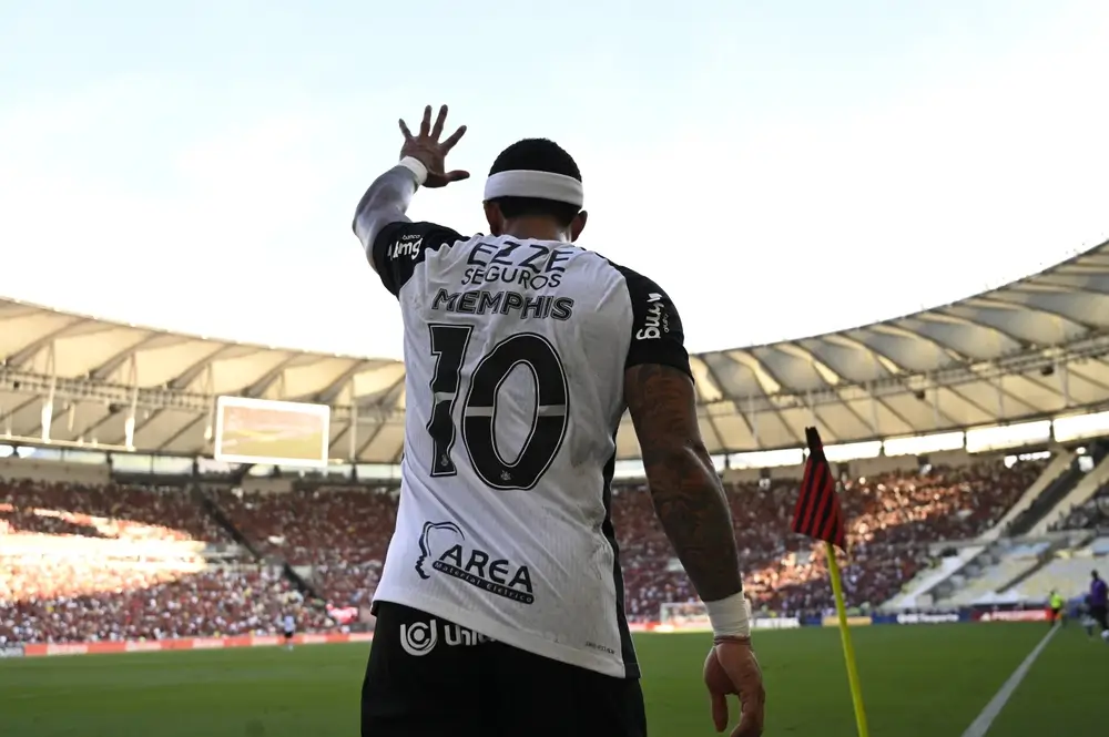 Jogador Memphis Depay, do Corinthians, aparece de costas levantando a mão para a torcida em estádio lotado durante partida, em imagem que ilustra discussões sobre o futuro do Memphis Depay no Corinthians.