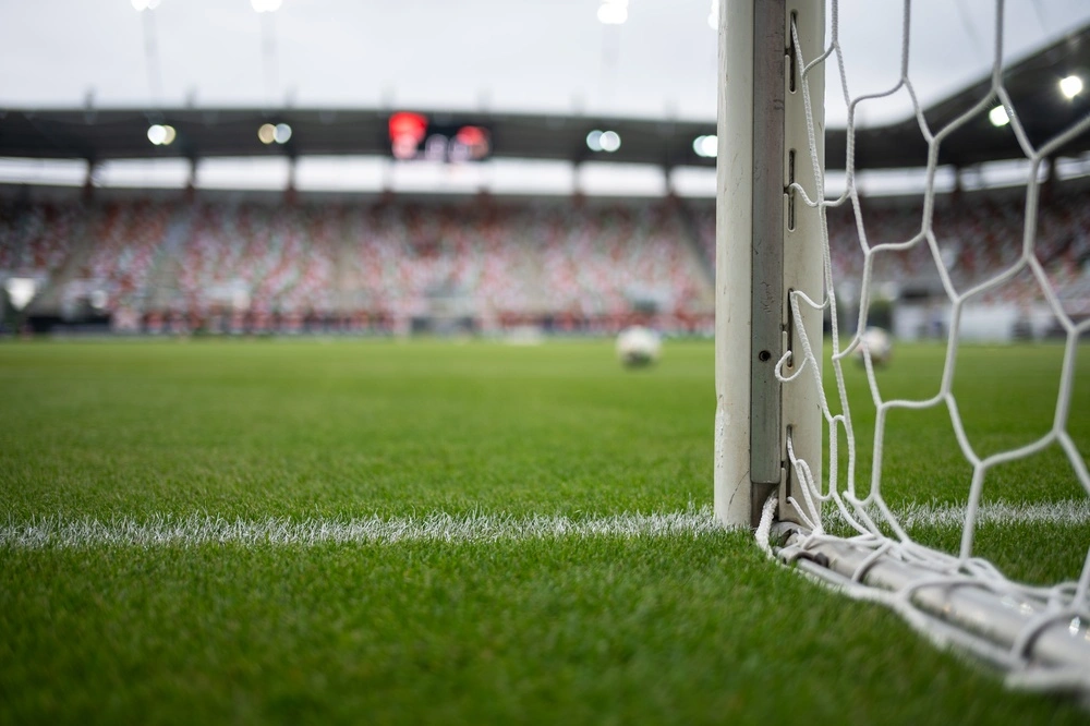 Foto de uma trave de futebol com rede em primeiro plano e estádio desfocado ao fundo, ilustrando o tema quantos gols jogadores do Corinthians fizeram em Copas do Mundo, com gramado verde e ambiente de partida profissional.
