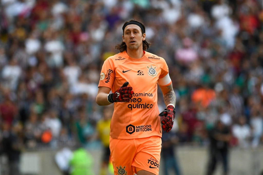 Goleiro Cássio do Corinthians com uniforme laranja em campo, durante partida com torcida desfocada ao fundo, em imagem sobre ídolos do Corinthians em Copas do Mundo.