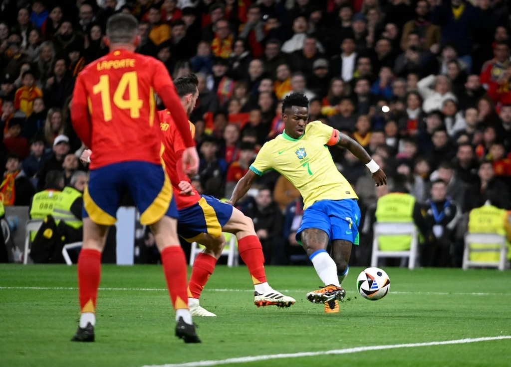 Apostas Copa do Mundo 2026 em lance entre Brasil e Espanha, com Vinicius Jr. da Seleção Brasileira conduzindo a bola durante partida em estádio lotado.